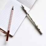 Flat lay of a notepad with two decorative pens on a white surface, ideal for stationery themes.
